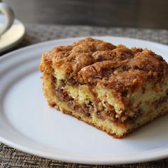 a piece of coffee cake on a white plate next to a cup and saucer