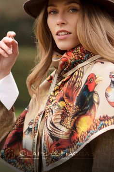 Woman wearing a colorful scarf with a pheasant design and a brown hat outdoors.