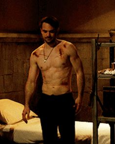 a shirtless man standing in front of a bed with blood all over his body