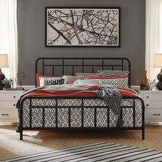 a black metal bed frame with red pillows and blankets on it in a bedroom setting