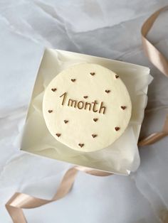 a white cake with the word 1 month on it sitting in a gift box next to a ribbon