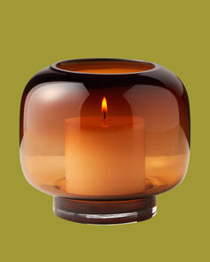 a candle that is inside of a glass container on a green background with an orange light in the middle