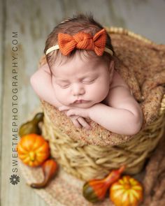 a baby sleeping in a basket with an orange bow