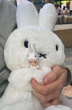 a person holding a white stuffed animal in their hands with the face of a rabbit on it's chest