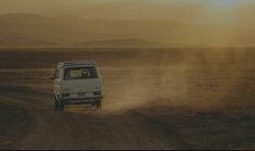 a white van driving down a dirt road in the middle of an open desert area