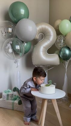 a young boy standing in front of a cake with balloons behind him and the number 25 on it