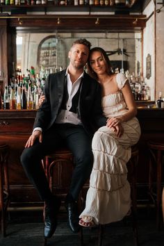 a man and woman sitting next to each other in front of a bar