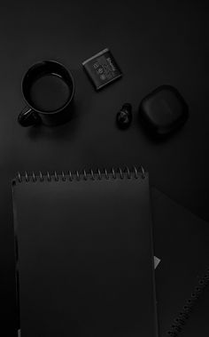 a black desk with a notepad, coffee cup and headphones