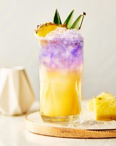 a tall glass filled with purple and yellow liquid sitting on top of a wooden board