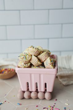 a pink container filled with cupcakes and sprinkles on top of a table