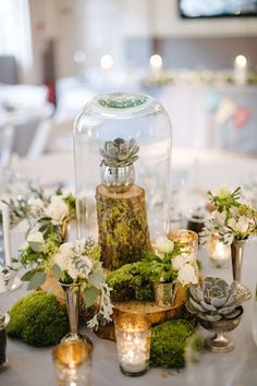 an arrangement of flowers and candles on a table with a glass clochet cover