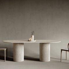 a white table with two chairs and a vase on the top, in front of a gray wall