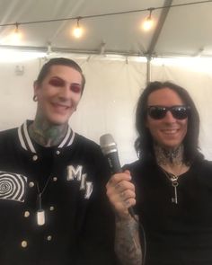 two people standing next to each other in front of a white tent holding microphones