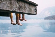 two feet hanging off the edge of a dock over water