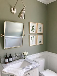 a bathroom with green walls and pictures on the wall above the sink, toilet and mirror