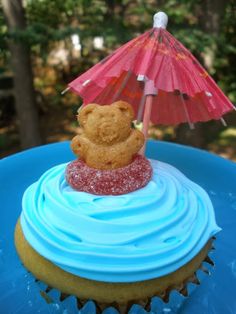 a cupcake with blue icing and a teddy bear on top is sitting under an umbrella