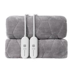 two remote controls sitting on top of gray blankets with white cord plugged into them