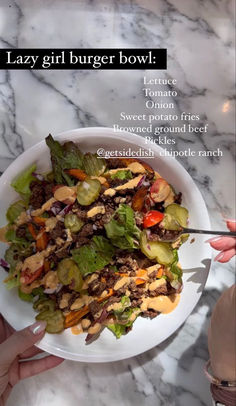 a person holding a white plate with salad on it and the words lazy girl burger bowl