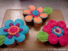 three cupcakes decorated with colorful frosting and flowers on top of a tray