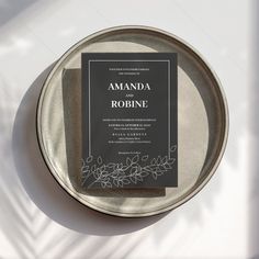 an elegant black and white wedding card on a silver plate with greenery around it