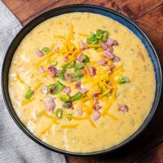 a bowl of soup with cheese, green onions and ham in it on a wooden table