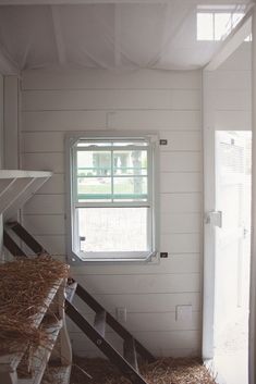 the inside of a house with hay on the floor and stairs leading up to an open window