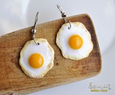 two fried eggs are sitting on top of a piece of wood with silver earwires