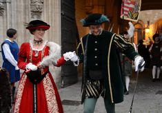 two people dressed in period costumes standing next to each other on the street with others walking by