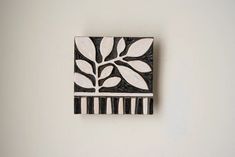 a white and black wall hanging on the side of a wall next to a plant