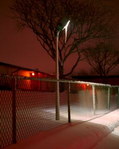 a street light on top of a pole in the middle of snow covered ground next to a fence