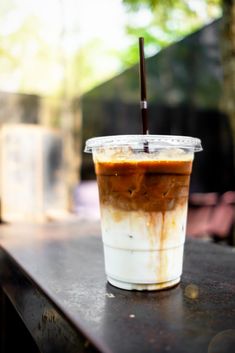 a plastic cup filled with liquid sitting on top of a wooden table next to a tree