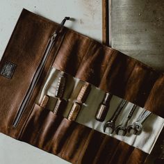 an assortment of tools are placed in a leather case on a table top with a zippered pouch