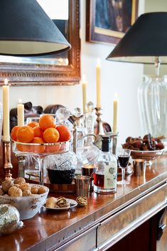 a wooden table topped with plates and bowls filled with oranges next to candlelight candles