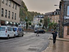 two people walking down the street in front of some buildings and cars on a rainy day