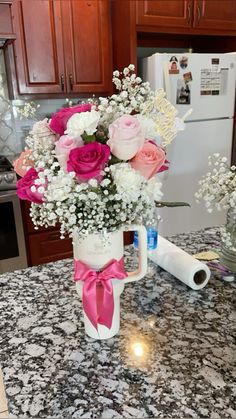 a vase filled with pink and white flowers sitting on top of a counter next to a roll of toilet paper