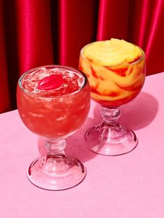 two glasses filled with drinks sitting on top of a pink table covered in red curtains