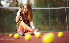 a woman sitting on the ground holding a tennis racquet and ball in front of her