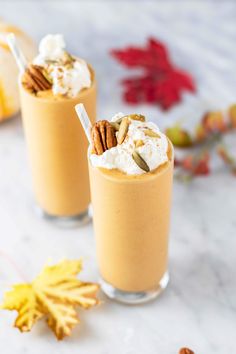 two glasses filled with pumpkin pie milkshakes and topped with whipped cream and pecans