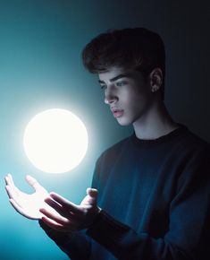 a young man is holding his hands out in front of the light that shines on him