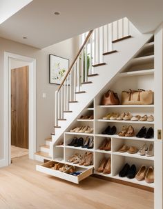 an organized closet under the stairs with shoes and purses on shelves in front of it