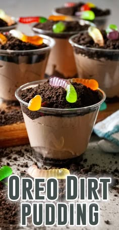 four cups filled with dirt sitting on top of a wooden table covered in dirt and candy