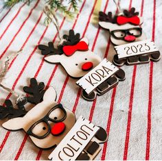 three reindeer magnets with glasses on them sitting on a striped tablecloth next to a christmas tree