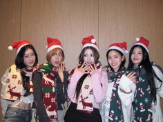 four young women wearing christmas sweaters and hats posing for a photo in front of a wooden wall