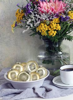 a vase filled with flowers next to a bowl of cookies and a cup of coffee