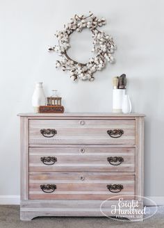 an old dresser with a wreath on the wall above it and other items sitting on top