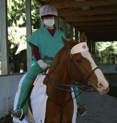 a person riding on the back of a brown horse wearing a medical mask and sitting on top of it