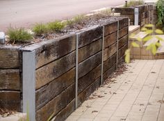 there is a wooden wall with plants growing out of it and on the side of the road