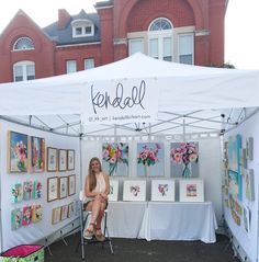 a woman sitting on a chair in front of a white tent with pictures and flowers