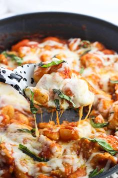 a spatula full of cheese and sauce being lifted from a skillet filled with pasta