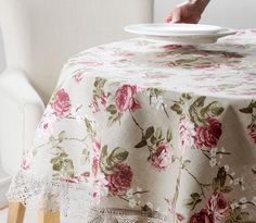 a table with a white plate on top of it and pink flowers on the table cloth